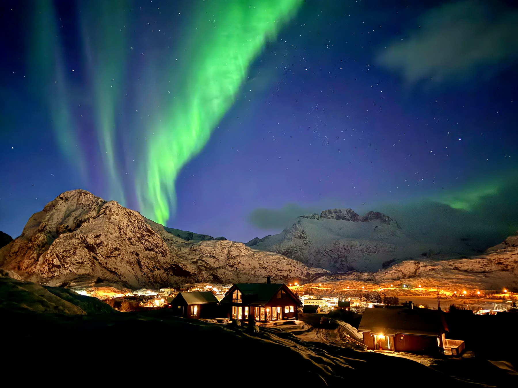 Nordlys over hyttetunet en vinternatt, med snødekte fjell i bakgrunnen